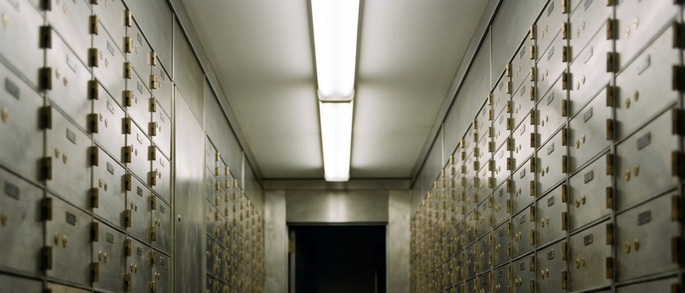Rows of safety deposit boxes inside a long narrow vault room under fluorescent light.